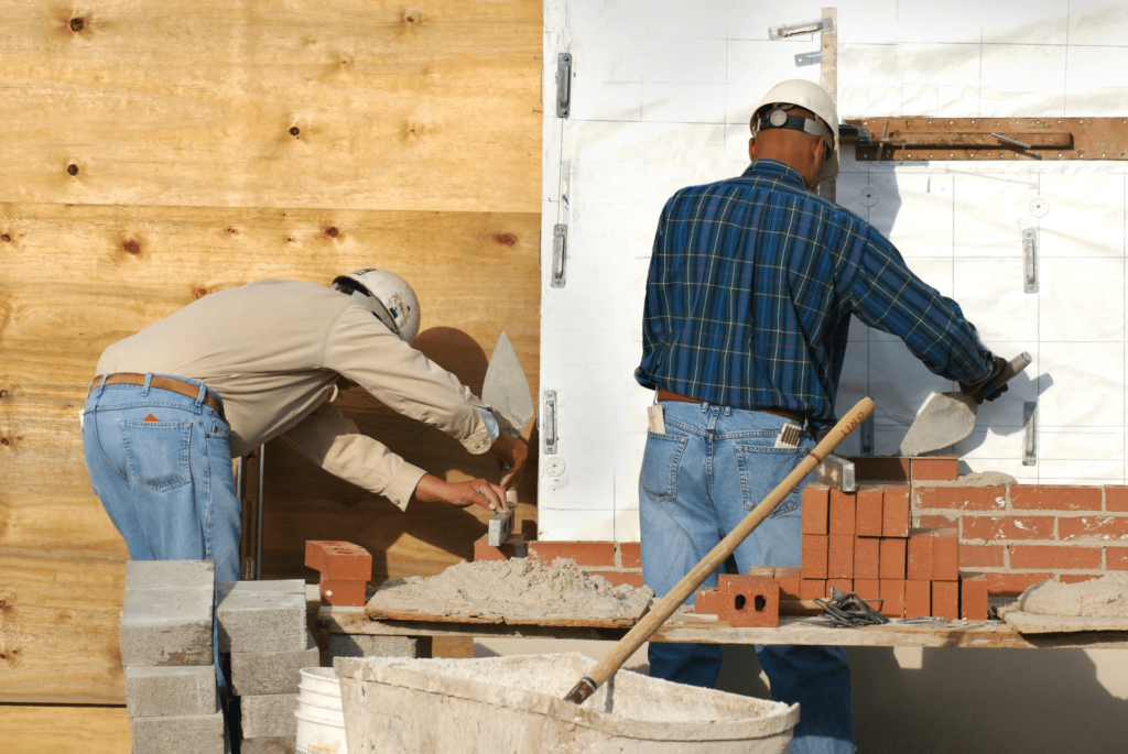2 masons building measuring and building a brick wall